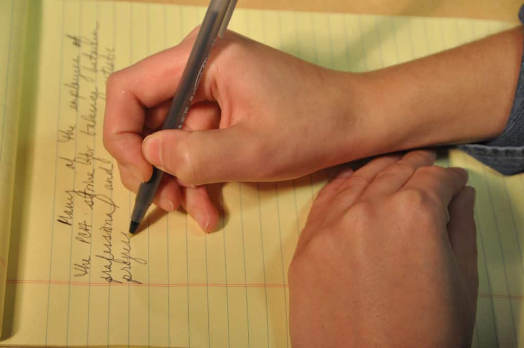 person writing on a yellow notebook